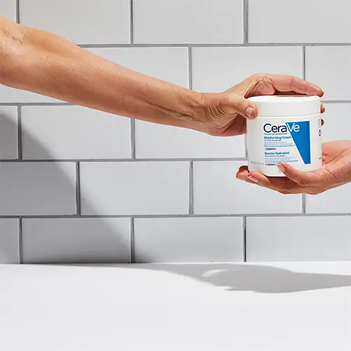 A hand reaching out to pass the CeraVe Moisturising Cream to another person